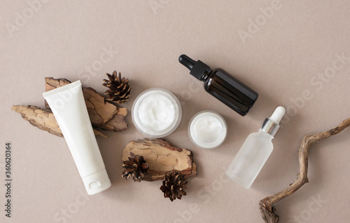 Set eco natural skin and body care beauty products and pine bark and cone on beige background flat lay, top view. Template plastic tube, glass jars and glass bottles with pipette photo