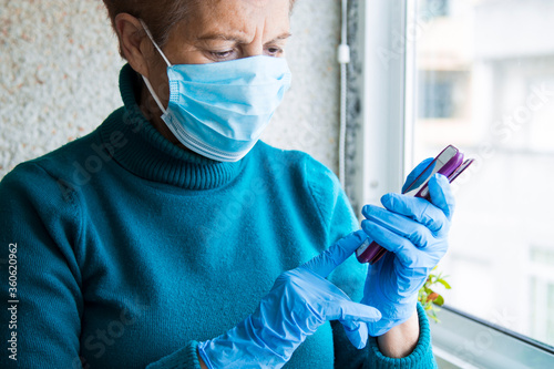 senior woman using mobile phone with mask and disposable medical gloves. Safety measures during the coronavirus outbreak