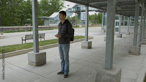 High quality picture of a young men who is walking outside on the street to to from parking lot on the train station. Handsome men carrying backback while rushing from to work.