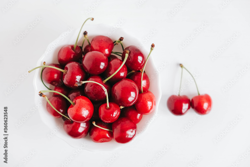 Fresh juicy red cherries in a white plate on the white wooden background. Top view. Copy, empty space for text Fresh juicy red cherries in a white plate on the white wooden background. Top view. Copy, empty space for text