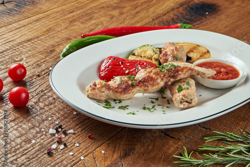 Appetizing rolls of Lyulya kebab - cooked from chicken minced meat in white plate with grilled vegetables. Wooden background photo