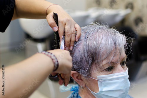 Manos de peluquera cortando el pelo a una mujer con el pelo blanco que lleva mascarilla