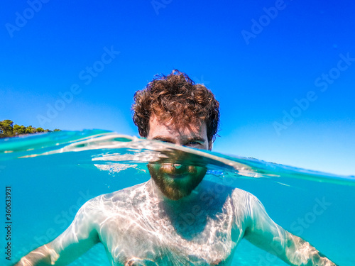 young spanish boy in the sea on the beach with his face half in and half out of the water with very clear skin, little sun cream