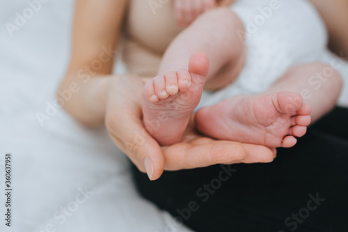 A loving, caring mother holds in her palm the legs of a small sleeping baby close-up. Woman's happiness. Photography, concept.