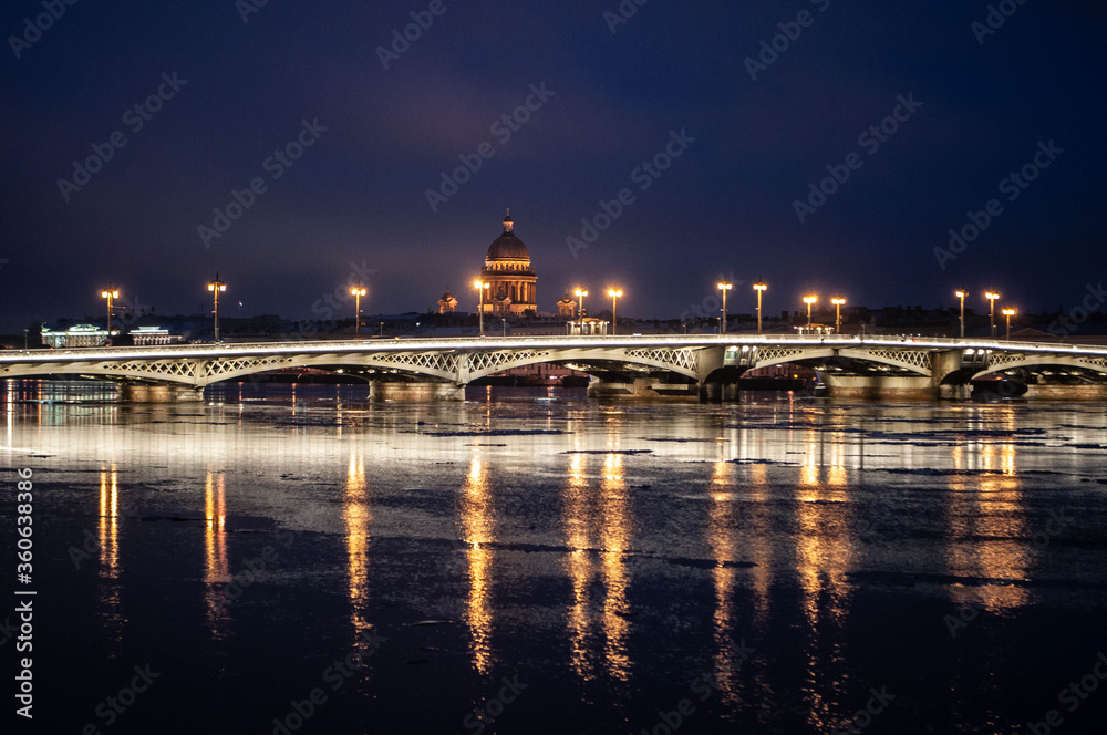 Enlighted Annunciation Bridge and Saint Isaac's Cathedral reflecting in The Neva river water at winter night. Landmark of Saint Petersburg, Russia.