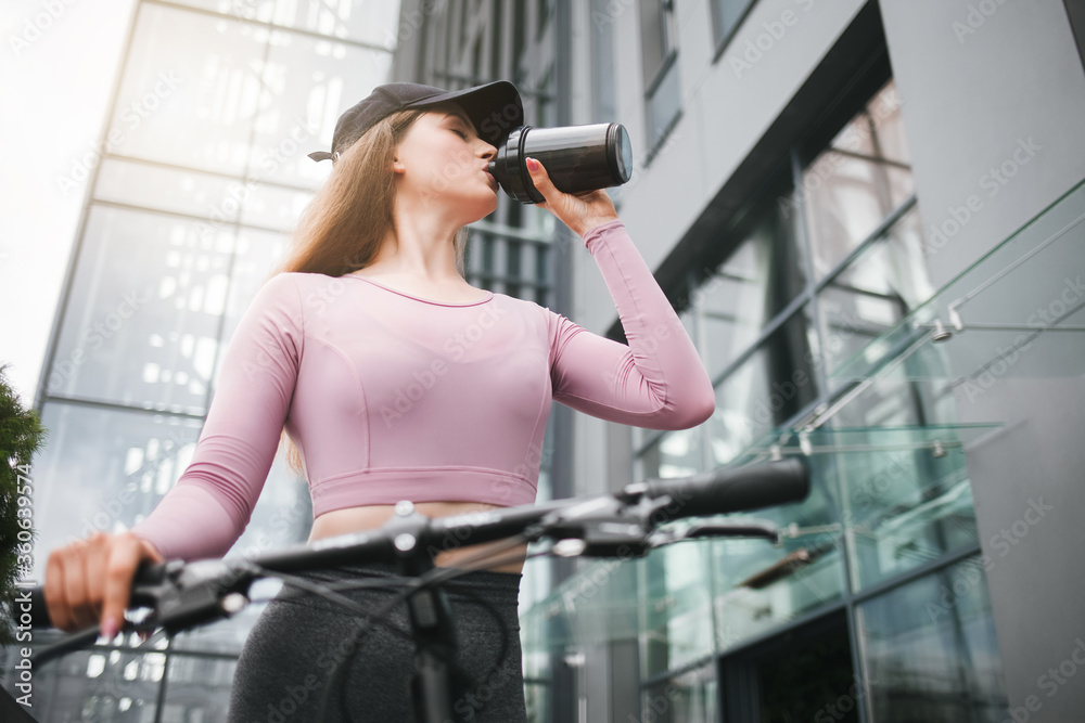 Girl on a bicycle drinks from a shaker after a long ride Girl on a bicycle drinks from a shaker after a long ride