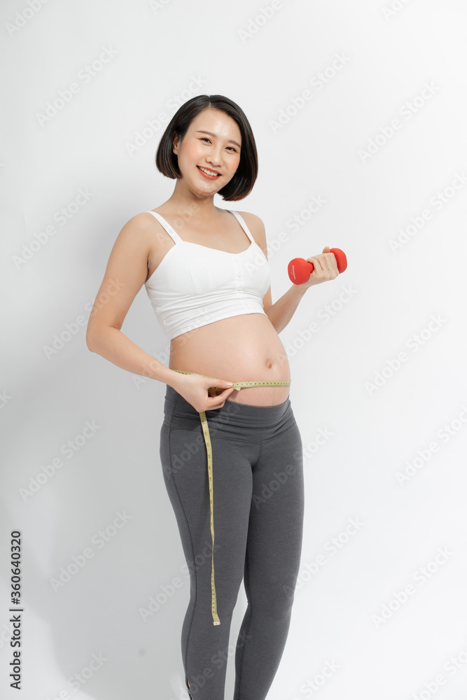 Young pregnant woman doing fitness and measuring belly with measuring tape Young pregnant woman doing fitness and measuring belly with measuring tape