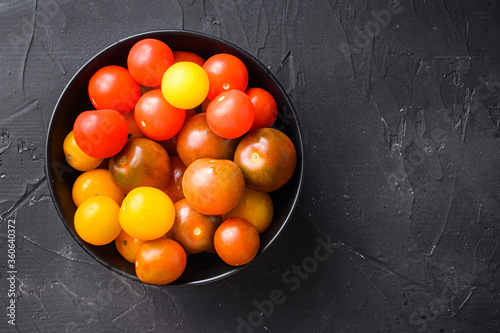 Cherry tomatoes in black bowl top view on black background space for text.