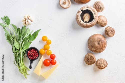 Ingredients for baking portobello, cheddar cheese, cherry tomatoes and sage on white background top view concept framed space for text.