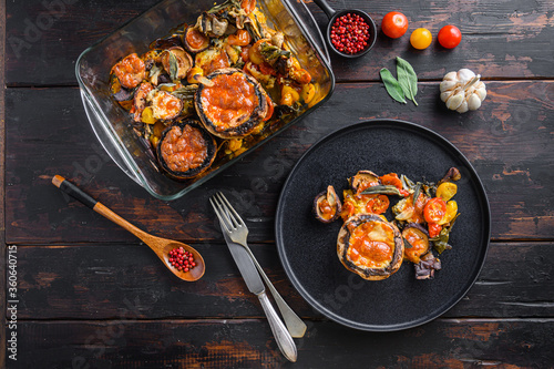 Fototapeta Naklejka Na Ścianę i Meble -  Served portobello  mushrooms,baked and stuffed with cheddar cheese, cherry tomatoes and sage on black plate over  old wooden dark background  top view