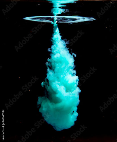 An abstract concept of teal color ink drop plume in the water on an isolated black background