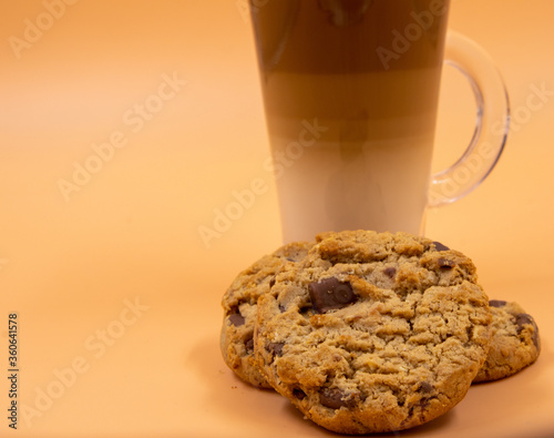 A studio shot of three-layered coffee drink and chocolate chip cookies in orange ombre background