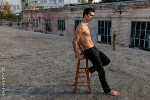 Profile portrait of a handsome sexy and fit sportive young man with naked torso, dressed in black jeans, posing on old abandoned factory.