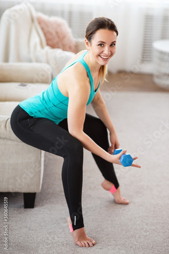 Smile woman exercising with dumbbells in living room. Full body workout at home.