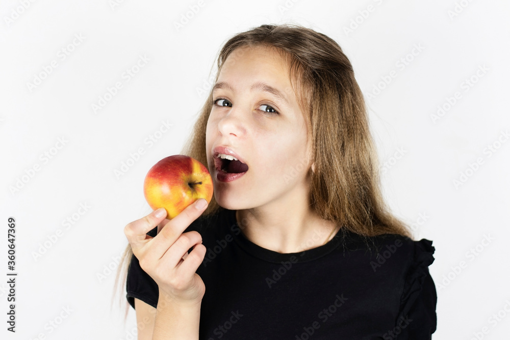 Beautiful young girl smiles and is going to eat a red apple, the girl loves to eat fruit, for her it is always a good snack Beautiful young girl smiles and is going to eat a red apple, the girl loves to eat fruit, for her it is always a good snack