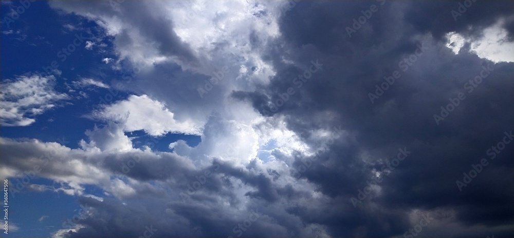 Fototapeta premium Rain clouds float over the small town, with sunlight passing through the soft white clouds.