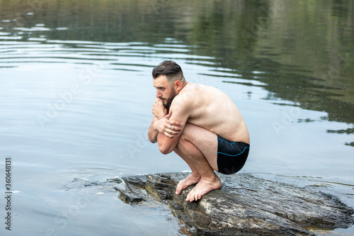 a person suffering from cold stands on a stone around water and nature