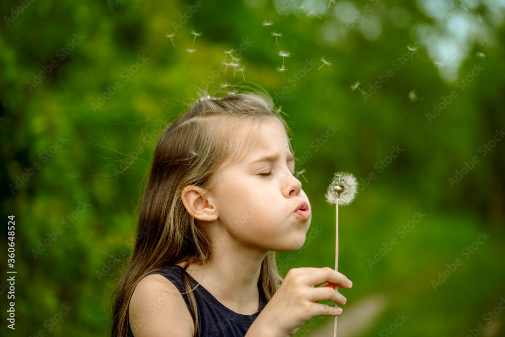 Summer in the park or forest. nature, freshness idea and freedom. happy childhood.Summer joy, little girl blowing dandelion at sunset near the river Summer in the park or forest. nature, freshness idea and freedom. happy childhood.Summer joy, little girl blowing dandelion at sunset near the river