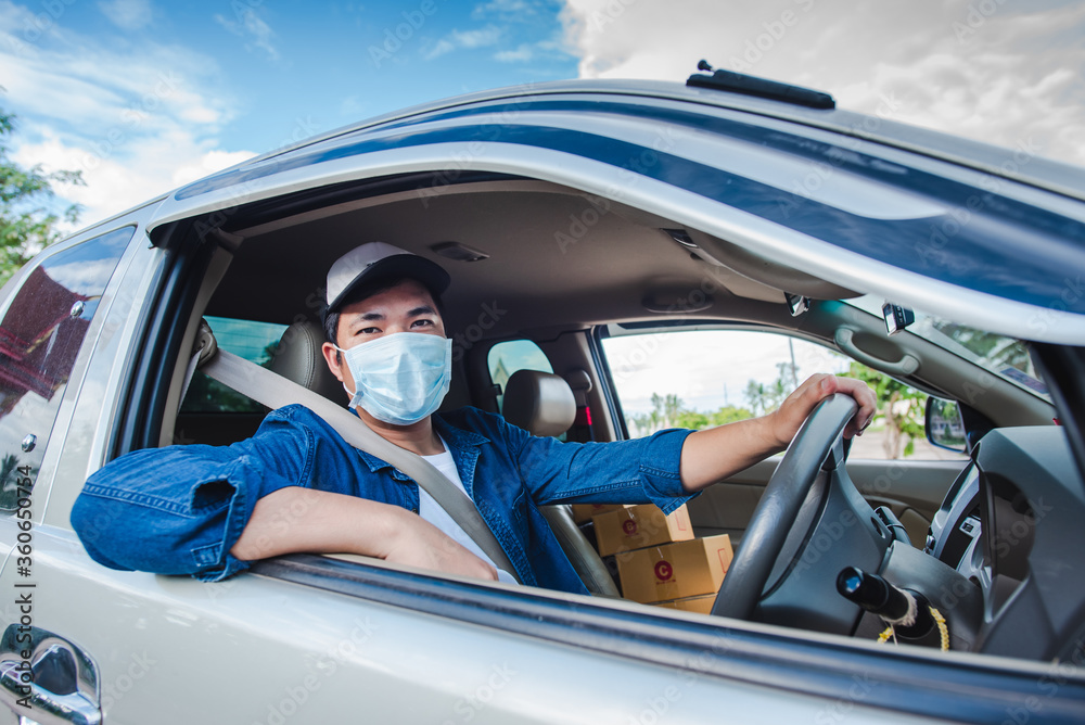 A young Asian man is a professional driving a package delivery car. Wear a medical mask Asians work to drive online deliveries to home. There is a parcel box in the car.