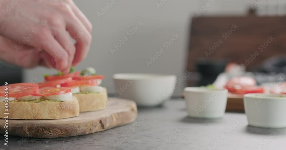 Slow motion dolly shot of young man making bruschetta with tomato, pesto and mozzarella on olive board Slow motion dolly shot of young man making bruschetta with tomato, pesto and mozzarella on olive board