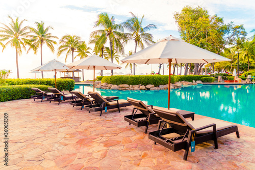 Fototapeta Naklejka Na Ścianę i Meble -  Umbrella and chair around swimming pool in resort hotel for leisure travel and vacation neary sea ocean beach