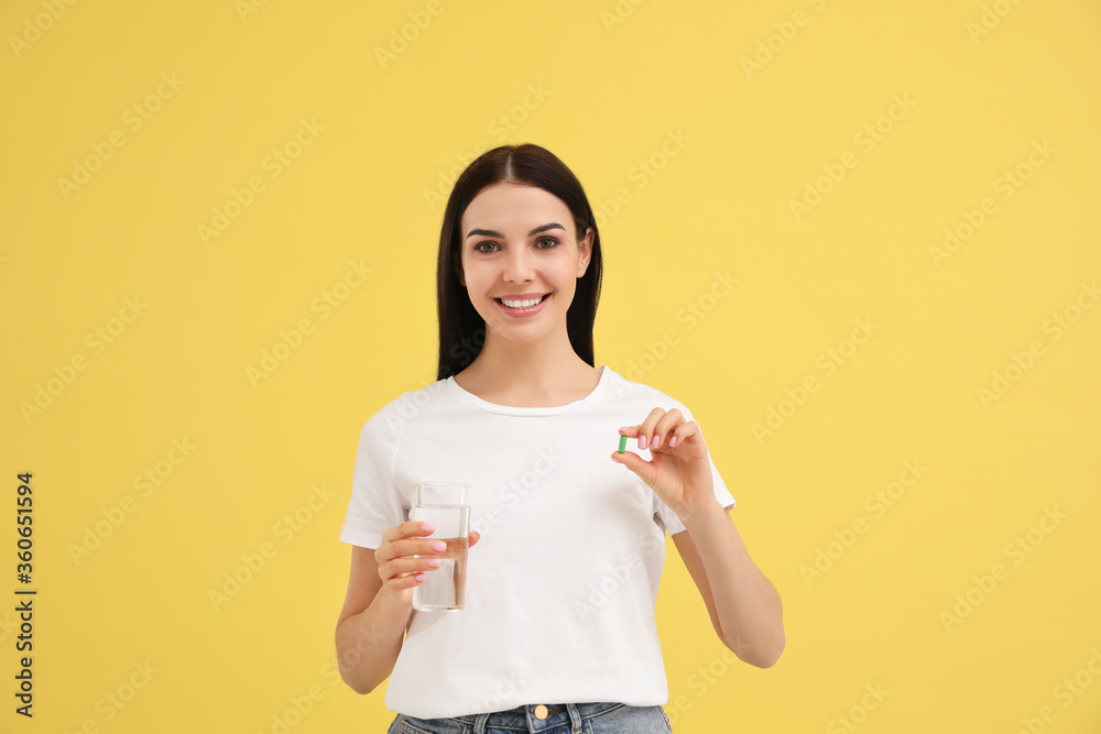 Young woman with glass of water and vitamin capsule on yellow background Young woman with glass of water and vitamin capsule on yellow background