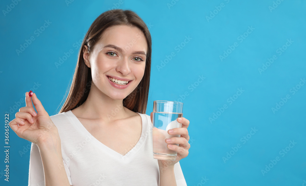 Young woman with vitamin pill and glass of water on blue background Young woman with vitamin pill and glass of water on blue background