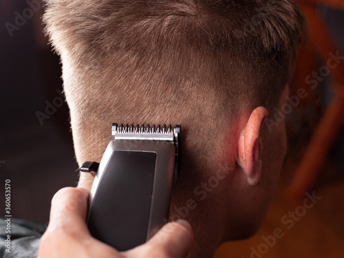 Men's haircut, master cuts r a young guy with a hair clipper close-up, hairdresser's tool