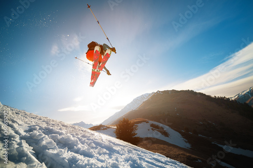 man skier in flight after jumping from a kicker in the spring against the backdrop of mountains and blue sky. Close-up wide angle. The concept of closing the ski season and skiing in spring