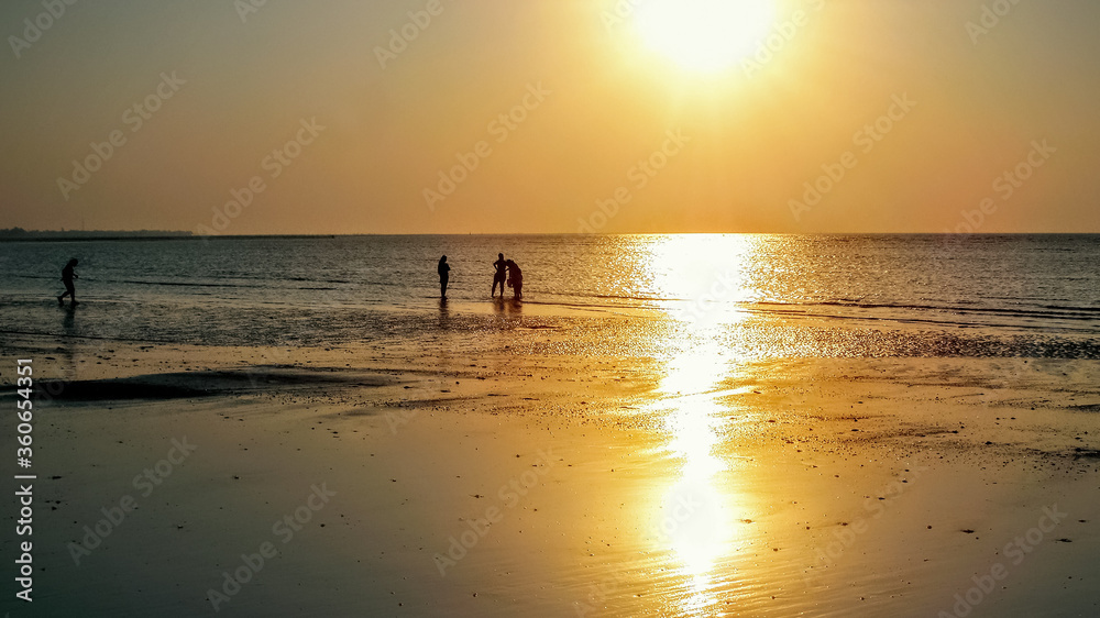 sunset at beach with people enjoying holidays with family playing in water