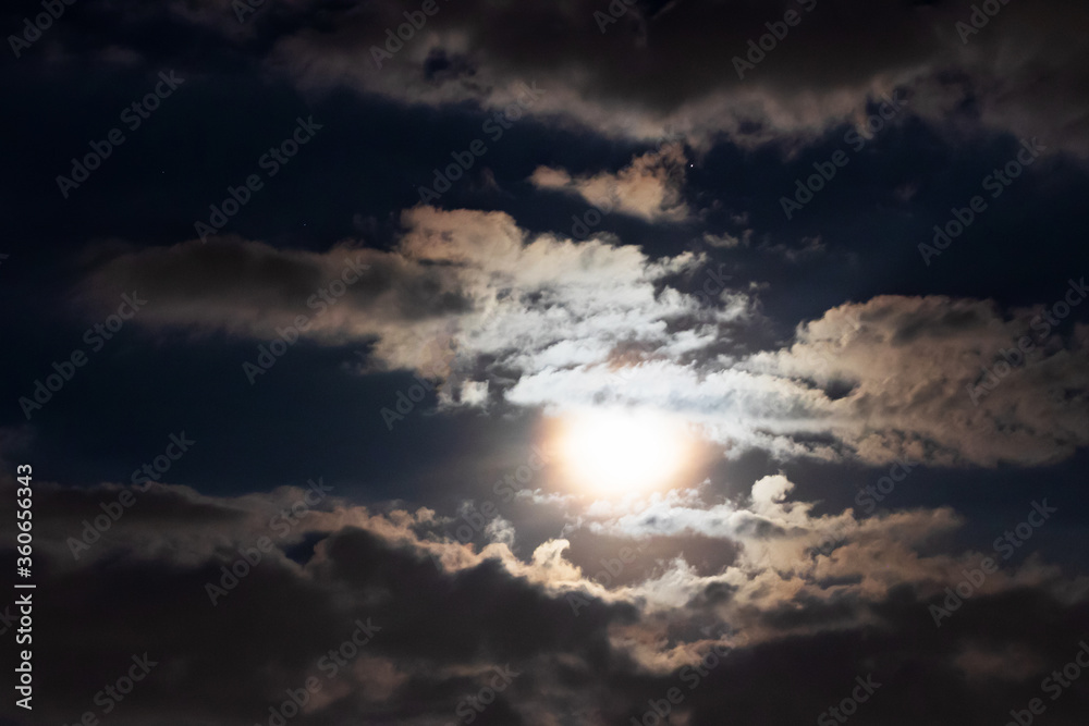 Full moon shining glowing light through the darkness of cloudy night sky; long exposure for beautiful nature background. Full moon shining glowing light through the darkness of cloudy night sky; long exposure for beautiful nature background.