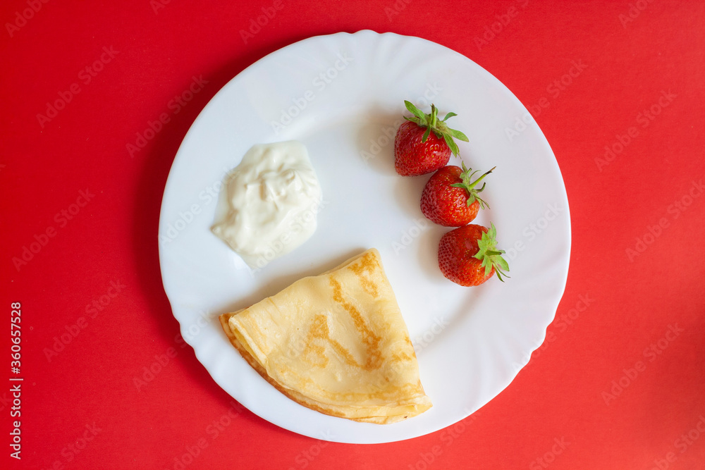 Breakfast, strawberries, pancakes and cream on a white plate on a red background Breakfast, strawberries, pancakes and cream on a white plate on a red background