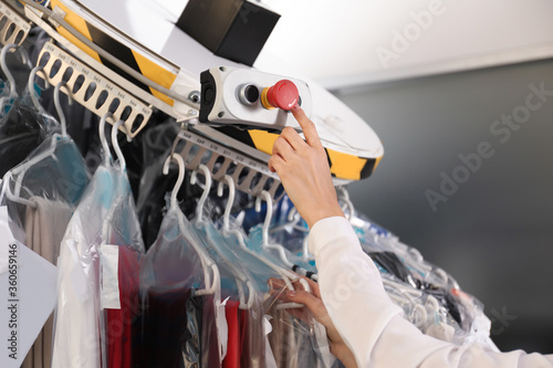 Obraz na plátne Worker pressing button on control panel of garment conveyor at modern dry-cleane