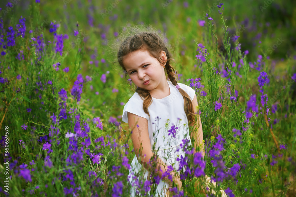 Portrait of a little girl in flowers . Happy child on a walk in the countryside