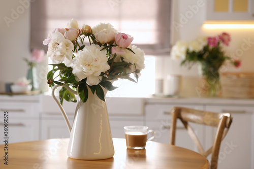 Beautiful peonies and cup of coffee on wooden table in kitchen