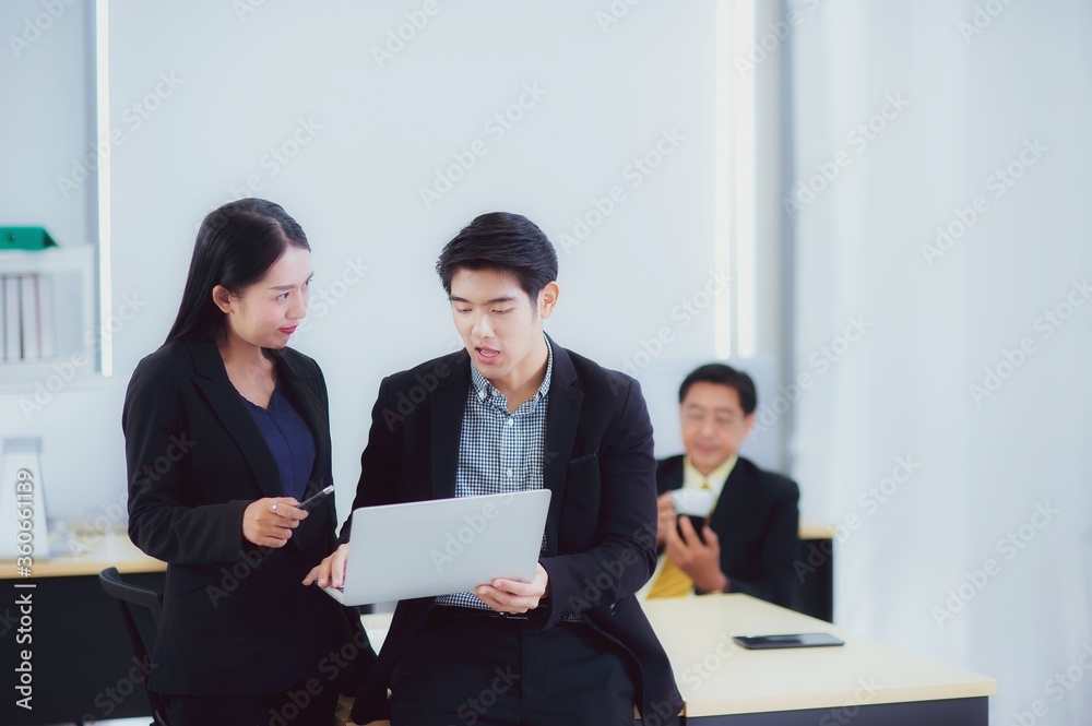 Happy young Asian Business people stand to discussing marketing information In the laptop computer in the office that looks modern, concept of teamwork of colleagues with happiness