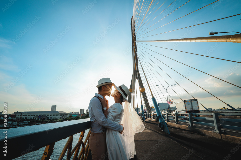 Wedding portrait of Asian couple kissing with sunlight on the bridge in the evening Wedding portrait of Asian couple kissing with sunlight on the bridge in the evening