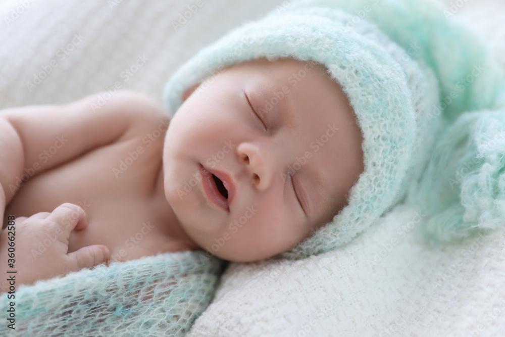 Cute newborn baby in warm hat sleeping on white plaid, closeup