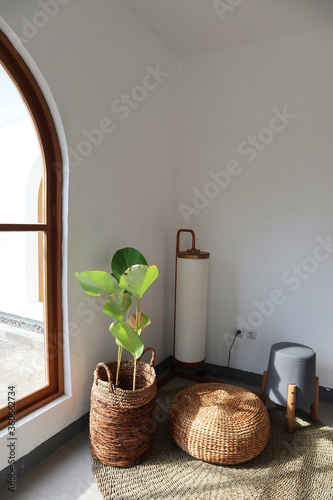 Aesthetic interior. Sitting corner has floor lamp, floor mat, plants and chair. Plants basket and chair made from water hyacinth. Sun shines through window