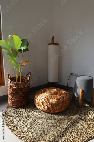 Aesthetic interior. Sitting corner has floor lamp, floor mat, plants and chair. Plants basket and chair made from water hyacinth. Sun shines through window