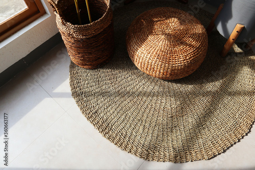 Aesthetic interior. Sitting corner has floor mat, plants and chair. Plants basket and chair made from water hyacinth. Sun shines through window