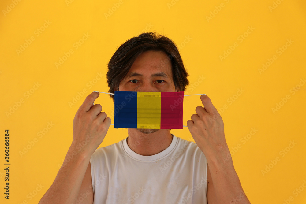 A man with Chad flag on hygienic mask in his hand and lifted up the front face on yellow background. Tiny Particle or virus corona or Covid 19 protection. A man with Chad flag on hygienic mask in his hand and lifted up the front face on yellow background. Tiny Particle or virus corona or Covid 19 protection.
