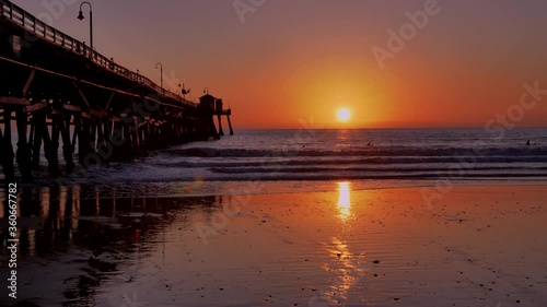 Scenic orange pink Sunset with epic rays of light and sun flare wooden pier in San Clementa California