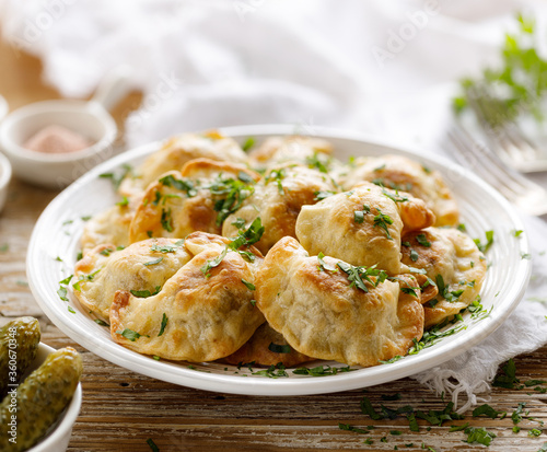 Baked dumplings stuffed with mushrooms and lentils sprinkled with fresh chopped parsley on a white plate on a wooden table, close up view