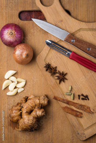 Spices with onion, garlic and ginger on wooden cutting board with knief and peeler. photo