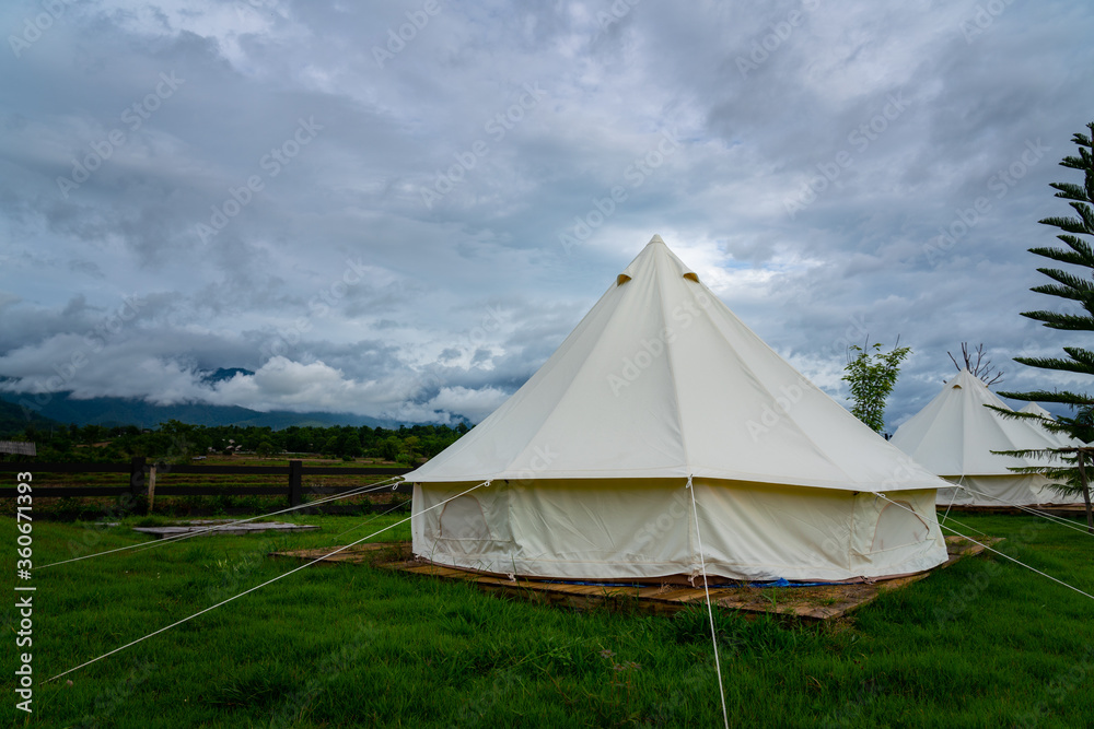 Canvas dome tent or Wigwam camping room at rural location with natural environment such as mountain valley, greenery garden and cloudy sky. Recreation outdoor activity photo concept.