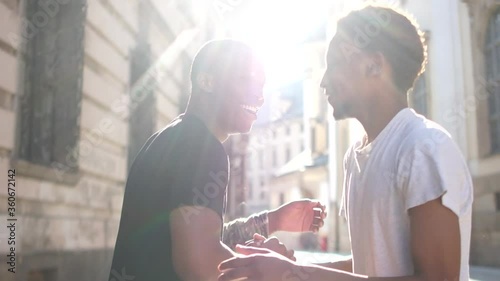 Two black guys greet each other at a meeting. Outdoor portrait African students greeting and hugging, sun glare. Brotherhood and Equality Concept photo