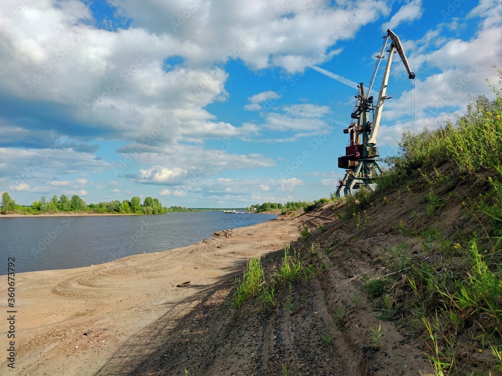 sandy river bank against the background of two high cranes and blue sky on a sunny day