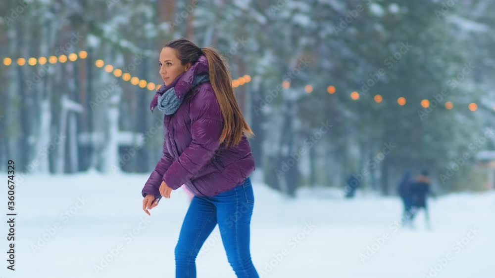 beautiful young lady with long ponytail in purple jacket spins on skates on outdoor rink in snowy winter park slow motion beautiful young lady with long ponytail in purple jacket spins on skates on outdoor rink in snowy winter park slow motion