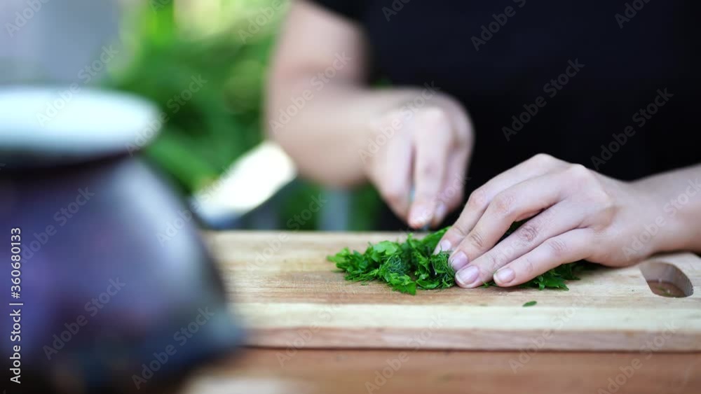 Woman cutting greens on wooden board outdoors. Close up of woman's hands cutting verdure with knife on chopping board.
